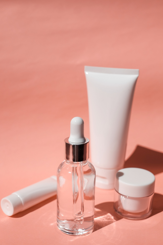Serum Bottle, Cosmetic Tubes and Container on Pink Background